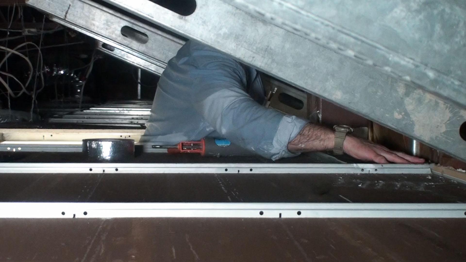 An installer adds a sheet of Ceiling Tile Barrier directly over existing ceiling tiles, taping down as needed