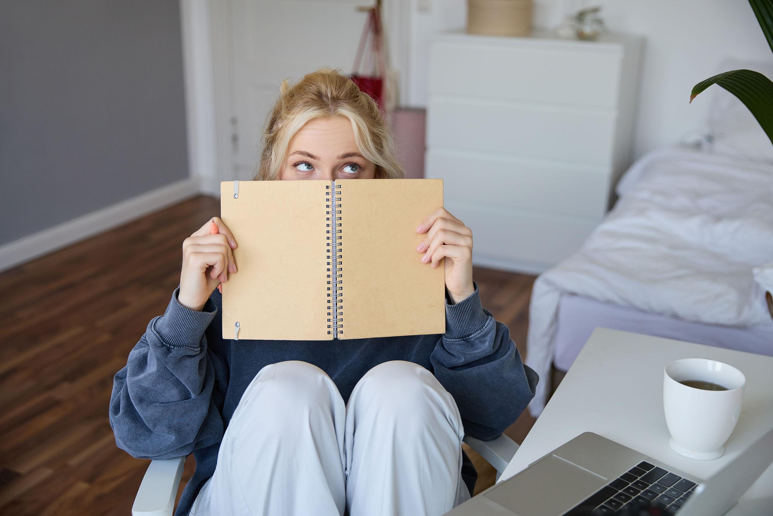 Blond woman hides her face with a notebook. Image by benzoix on Freepik