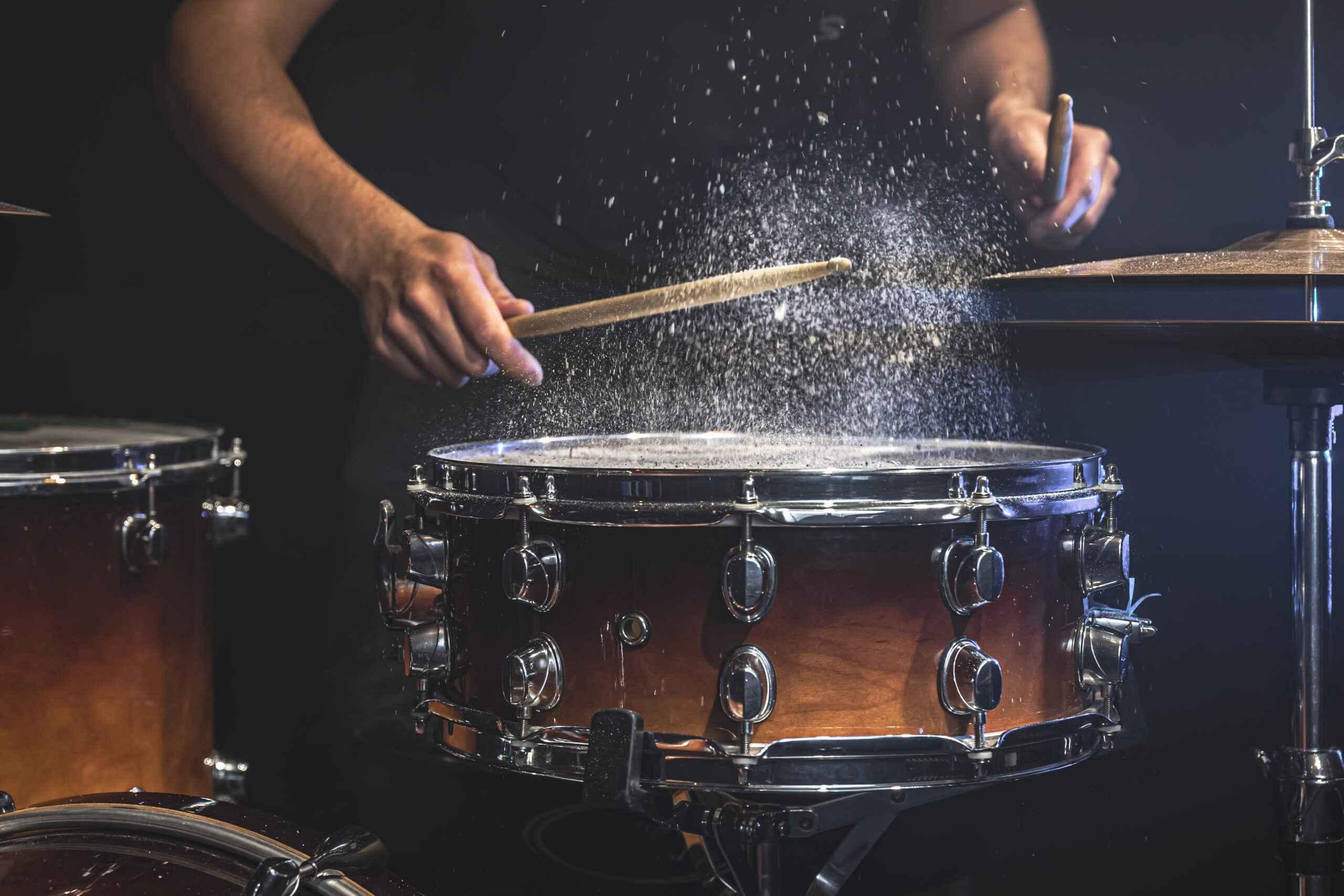 A male drummer plays snare drum with drumsticks in a dark room. Image by pvproductions on Freepik.