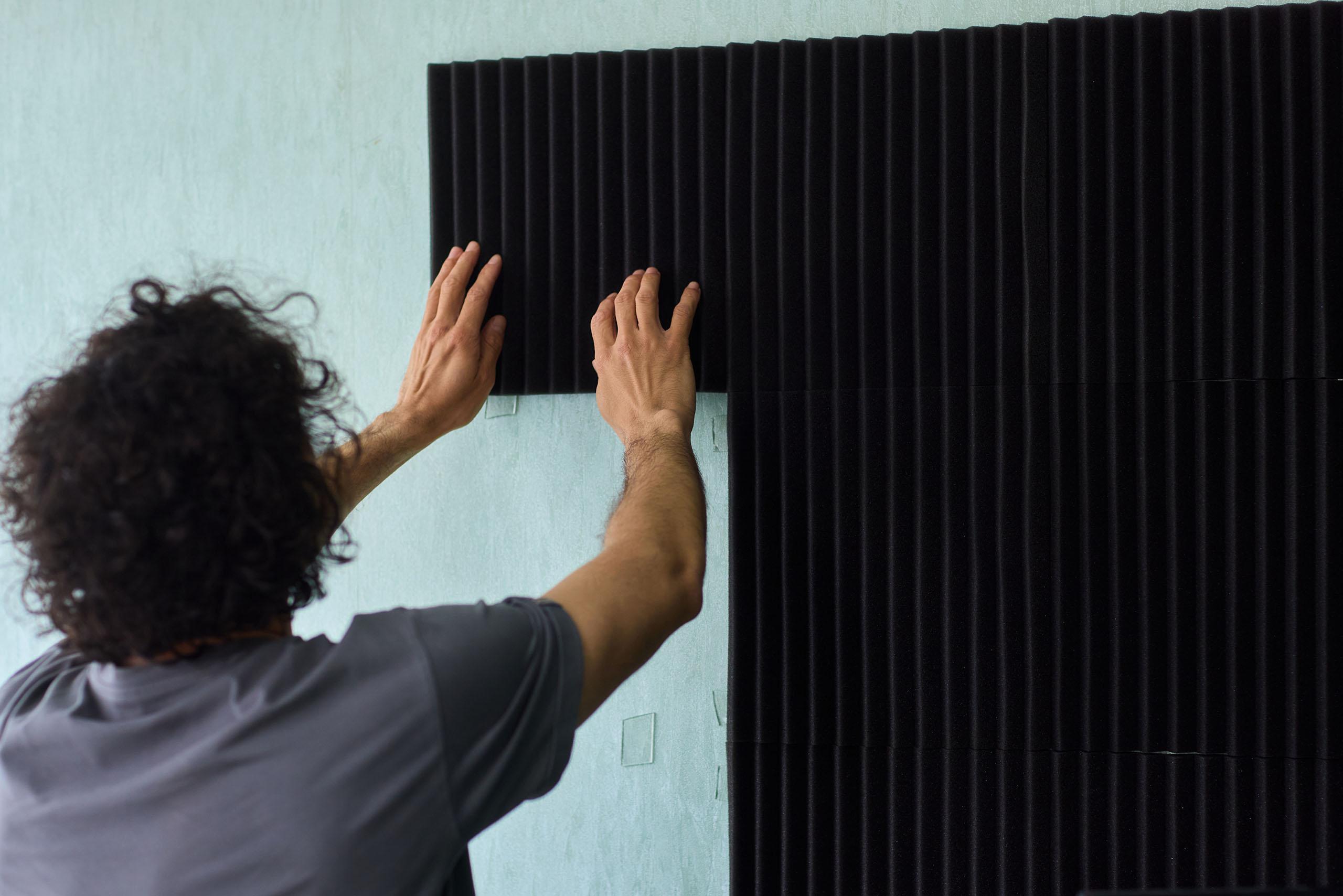 A man installs linear acoustic foam panels on a wall