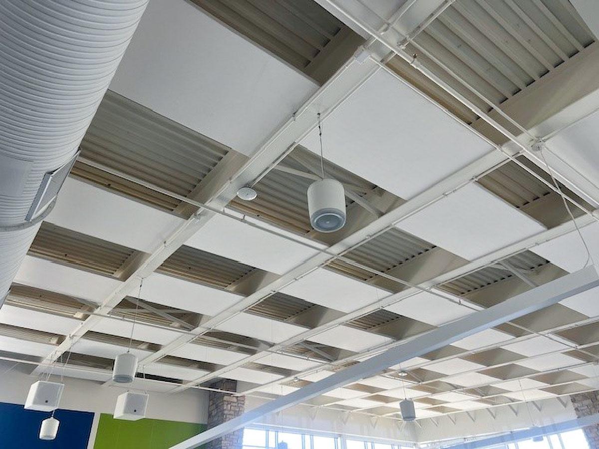 Fabric wrapped acoustic panels on the ceiling treat the acoustics in a school cafeteria.