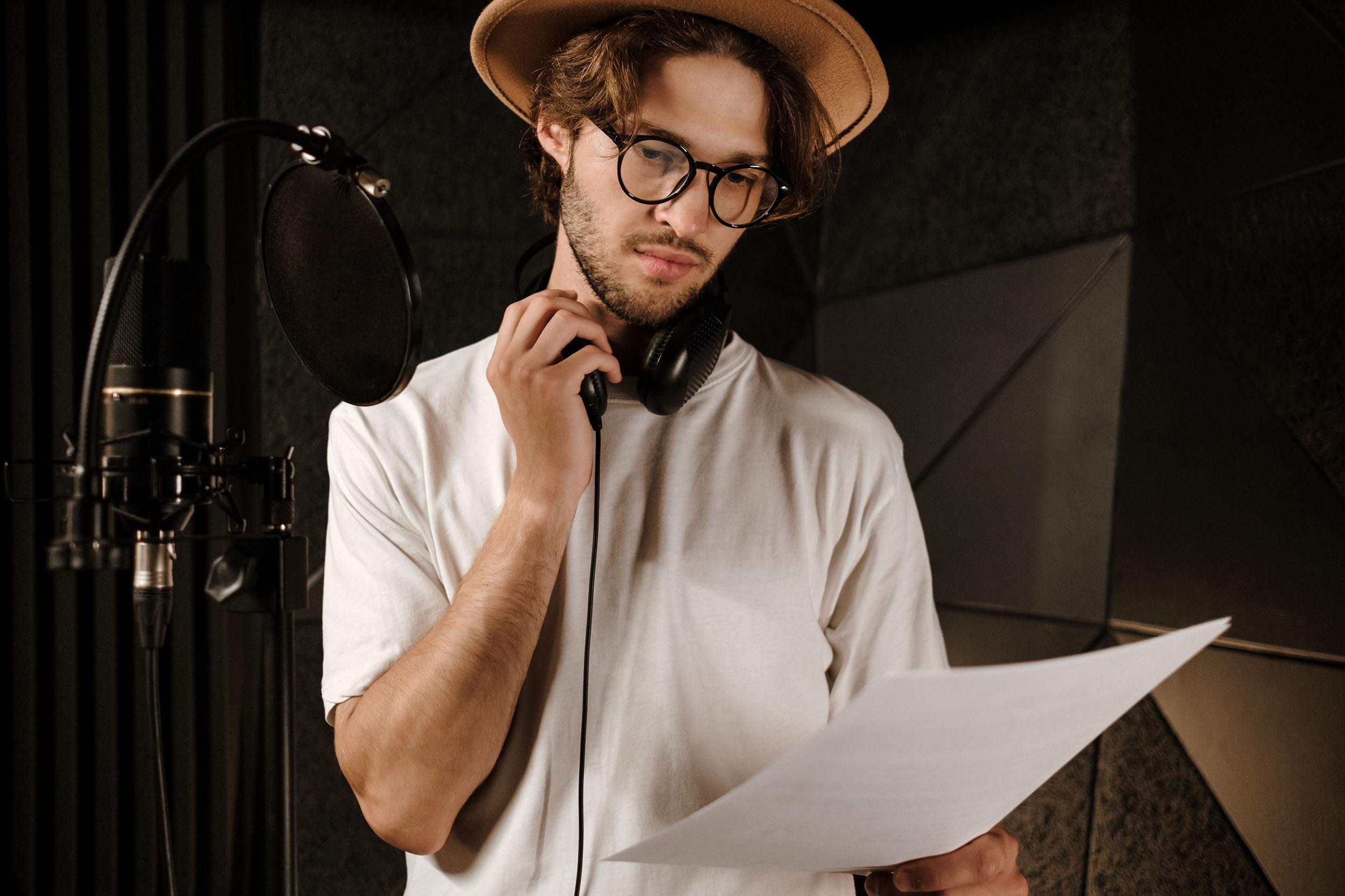Young confident male singer thoughtfully reading text of new song working in modern sound recording studio