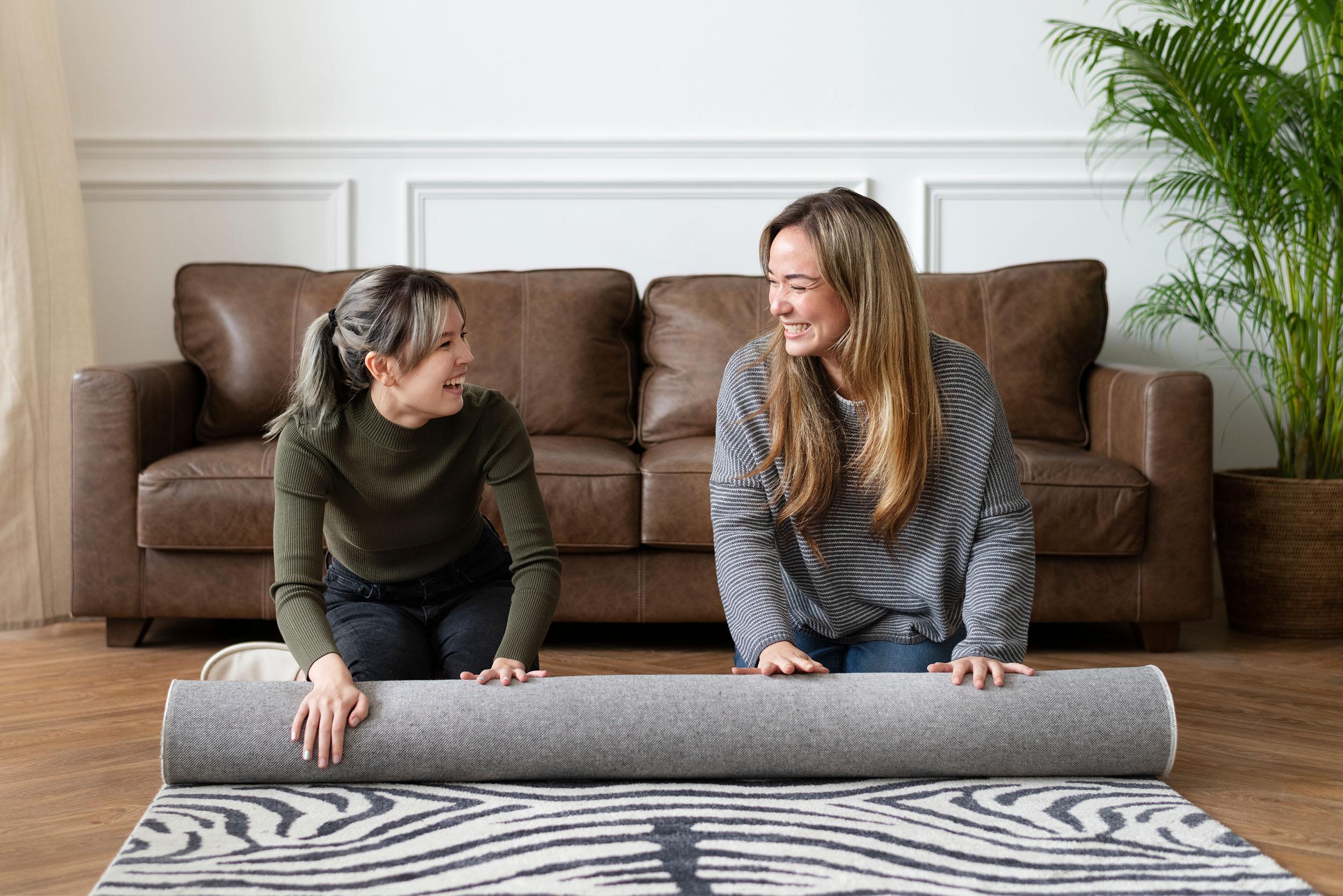 Two women roll up a rug. Photo by rawpixel on Freepik.
