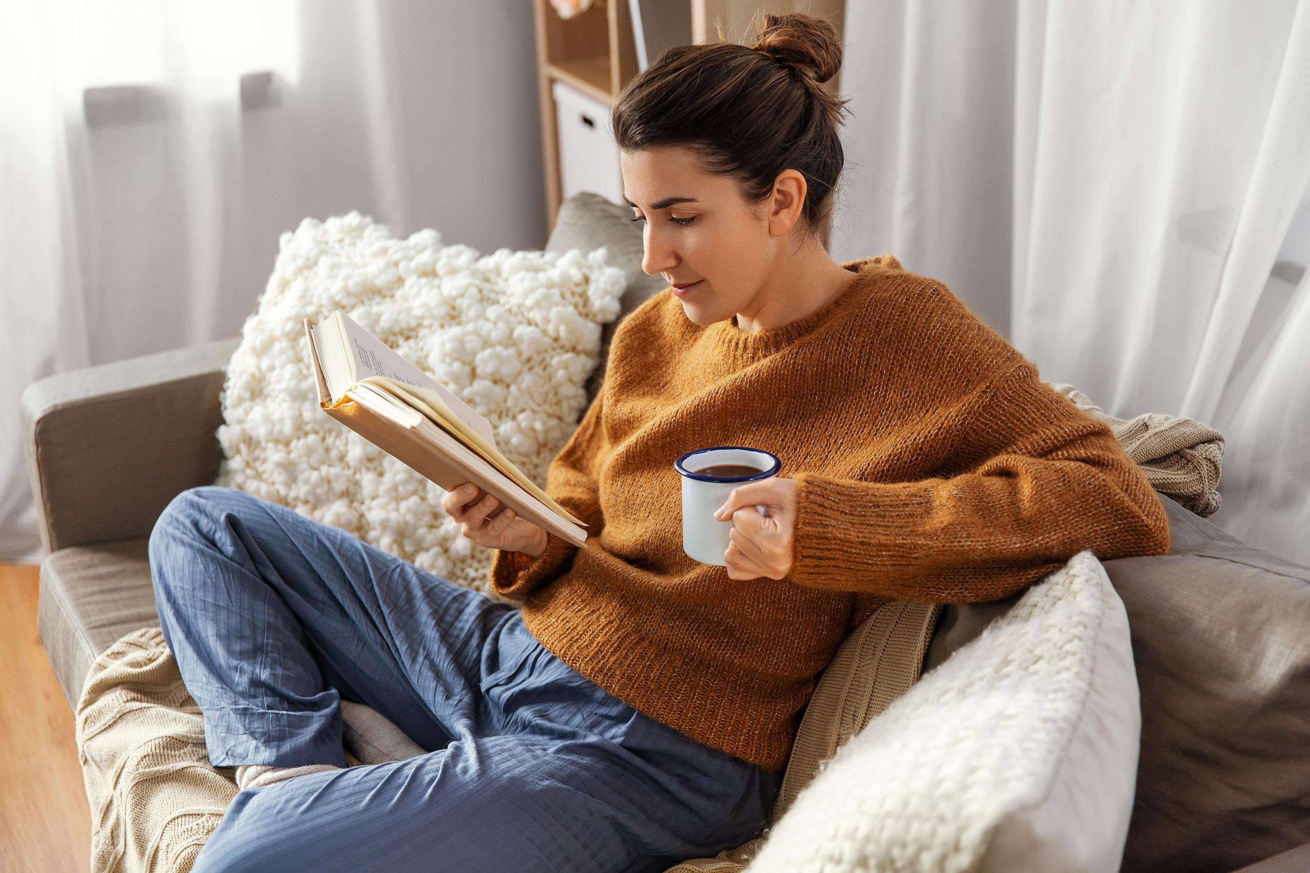 Woman drinking coffee while reading a book at her home