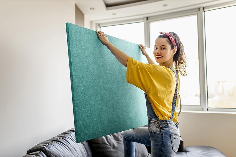 Woman wearing overalls holding fabric wrapped wall panel in a living room